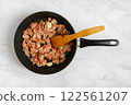 Cooking crispy bacon in a frying pan with a wooden spatula on a marble countertop 122561207