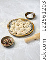 Freshly made dumplings arranged on a wooden plate with spices and rolling pin on a marble surface 122561203