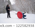 a child flips over from snow tubing while riding with his dad against the backdrop of a winter forest. Dangerous skiing in winter. Children's injuries during winter sports 122582938