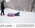 a child flips over from snow tubing while riding with his dad against the backdrop of a winter forest. Dangerous skiing in winter. Children's injuries during winter sports 122582939