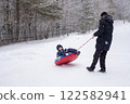 a child flips over from snow tubing while riding with his dad against the backdrop of a winter forest. Dangerous skiing in winter. Children's injuries during winter sports 122582941