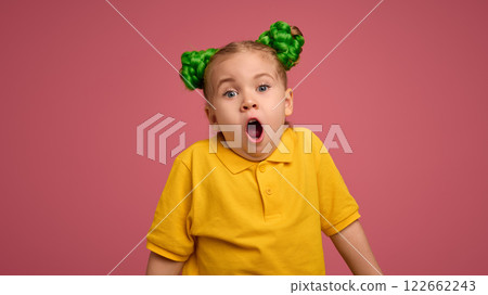 Portrait of adorable child, preschool girl wearing yellow polo shirt, with braided buns hairstyle making shocked face against pink studio background. 122662243