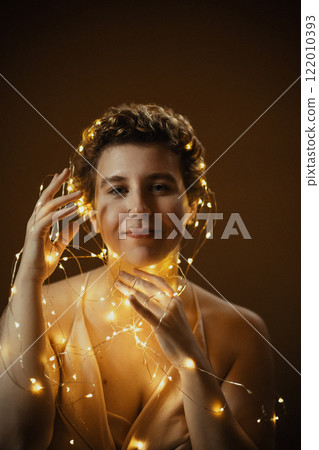 The soft glow of fairy lights illuminates the girl's serene head in a warm, intimate setting at dusk. 122010393