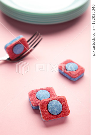 Dishwasher detergent tablet with fork and dishes on pink background. Vertical photo. 122023346