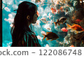 Asian young woman with dark hair female portrait in profile looking at the large aquarium with red fish. Leisure and entertainment. A girl in the zoo. 122086748