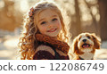 Little curly blonde girl walking with a dog in winter forest or park. A kid in sunny day have fun outdoors. Happy child with smiled face portrait.  122086749