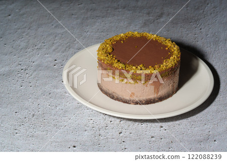 Dubai chocolate cheesecake with pistachio paste and kataifi dough filling covered in chocolate ganache on white plate. Gray background with copy space. Indulgence, gourmet desserts, art of culinary 122088239