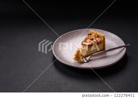 Delicious fresh cheesecake caramel peanut cake with cream and nuts on a ceramic plate on a dark concrete background 122276451