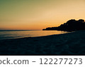 The seashore at sunset. Calm surface of the water in the doldrums against the orange yellow sky. Contrast landscape, the land in a shadow Sunset light 122277273