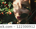 Close up portrait of a young woman plucking ripe red cherries from a tree in an orchard in summer. Harvesting, gardening, farming. Sun rays on a face. 122300912