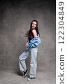 beautiful and long haired woman in stylish clothes posing in a photo studio and smiling. the model stands and poses in denim and sneakers on a gray photo background. 122304849