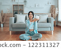 Young Asian woman holding piggy bank and sitting on the floor at home 122311327