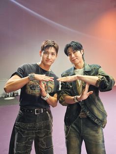 two young men standing next to each other in front of a purple wall holding their hands together