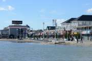 people are walking on the beach near some buildings and water in front of them,