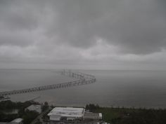 an aerial view of a bridge over the ocean on a cloudy day with dark clouds