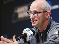 a man with glasses sitting at a table in front of a microphone and talking to someone