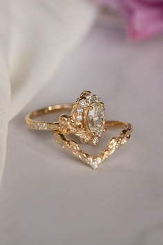 two gold rings with diamonds on them sitting next to a pink rose and white cloth