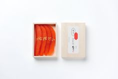 an open box with carrots in it on a white surface, next to a piece of paper