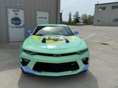 a green sports car parked in front of a building with graffiti on it's hood