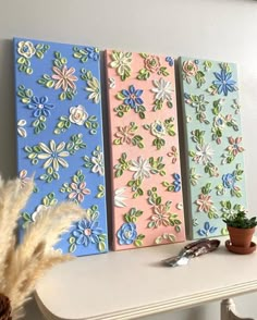 three canvases with flowers painted on them sitting on a table next to a potted plant