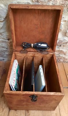 an open wooden box with several electronic devices in it on a wood floor next to a stone wall