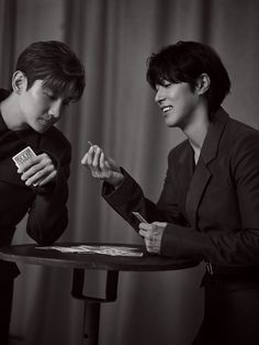 two people sitting at a table with cards in their hands and one person standing next to them