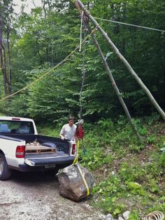 a man standing next to a pickup truck in the woods with a crane on it's back