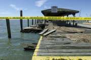 a yellow caution tape is on the side of a pier near water and boats in the background