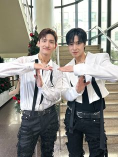 two young men standing next to each other in front of stairs and christmas wreaths