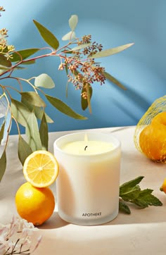 a white candle sitting on top of a table next to oranges