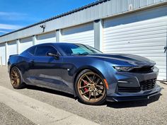 a gray camaro is parked in front of a garage door and two white garage doors