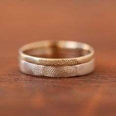 two wedding rings with fingerprints on them sitting on a wooden surface, close up