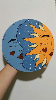 a hand holding up a paper plate with the sun and moon painted on it's face