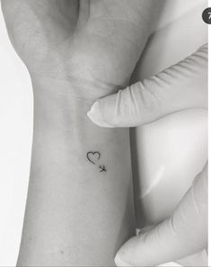 a small heart and an arrow tattoo on the left wrist is shown in this black and white photo