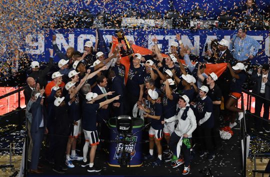 the men's basketball team celebrates with their trophy and confetti