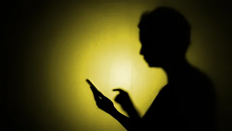 A silhouette against a yellow light of a person about to press down on a phone screen (Credit: Getty Images)