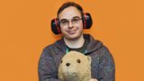 Photo of Jamie smiling, wearing large headphones and holding a toy lion.