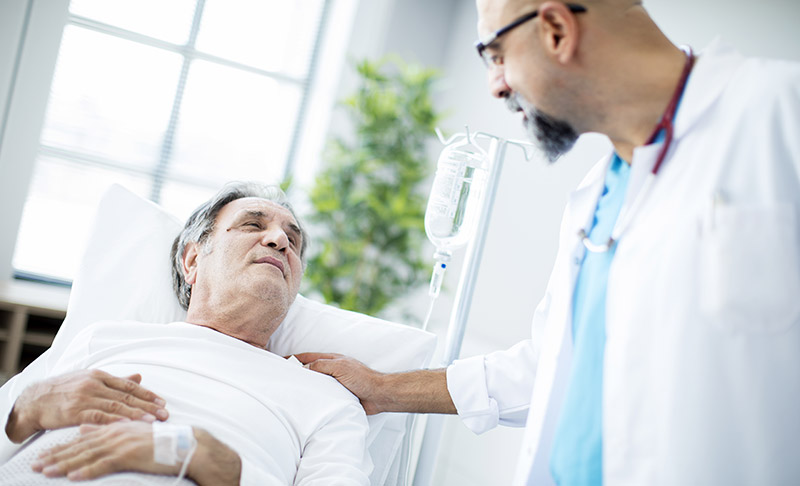 A healthcare provider with a hand on the shoulder of a patient lying in bed