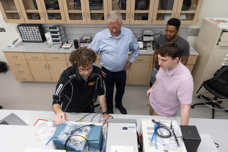 Three students show one adult the display on a piece of equipment