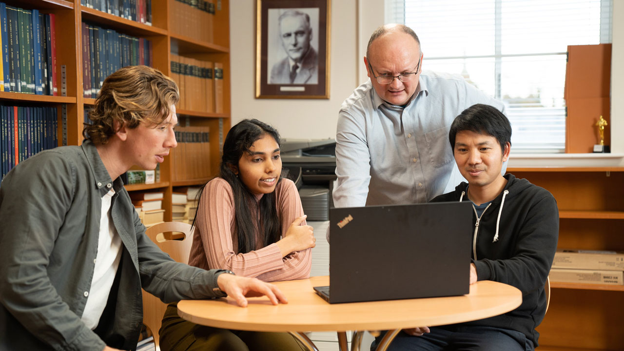 Four people sat around a laptop on a round wooden table