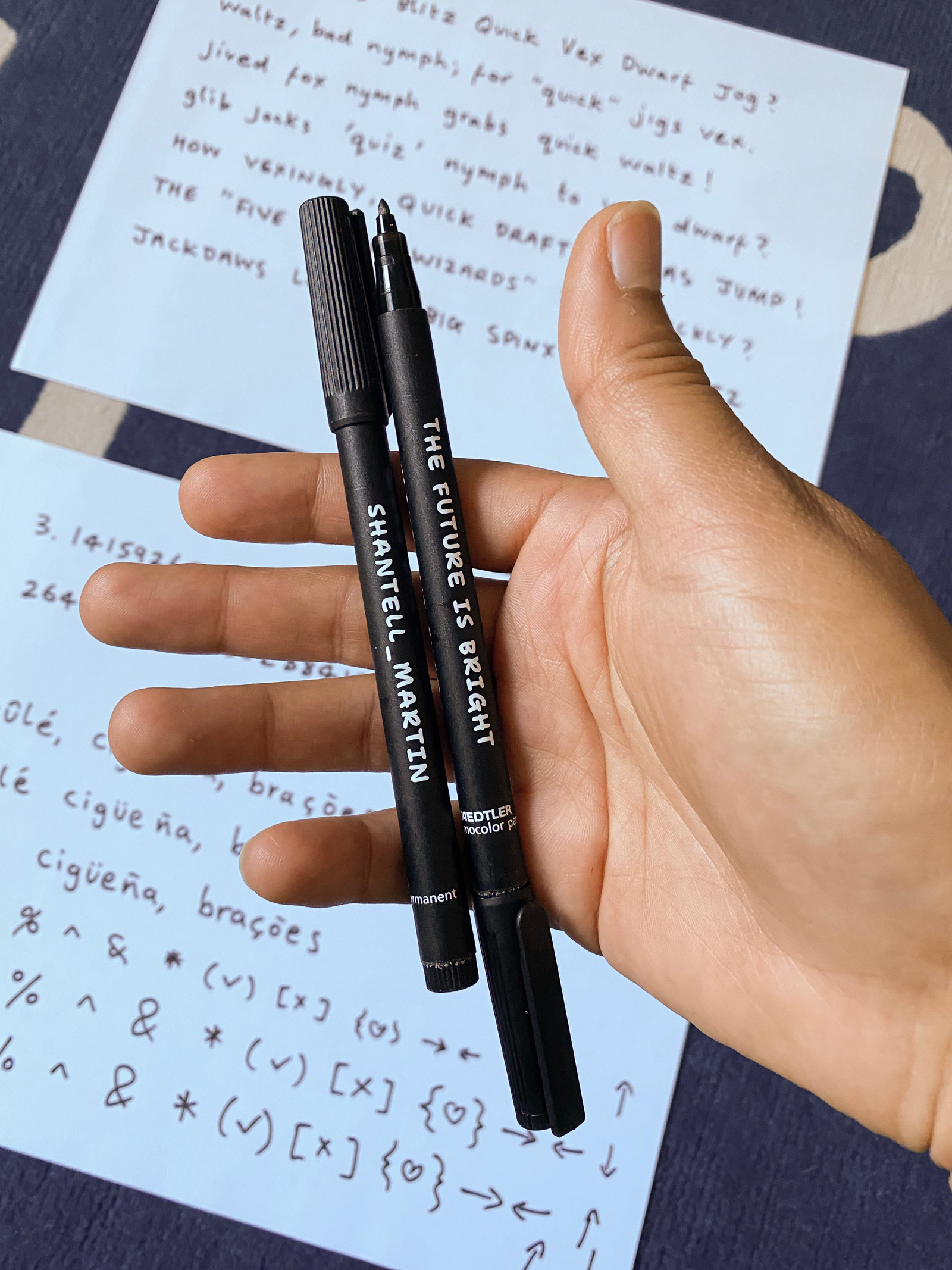 Shantell Martin holding Staedler markers, with handwriting samples in the background