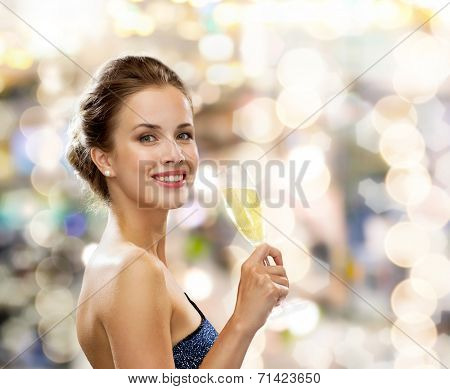 party, drinks, holidays, luxury and celebration concept - smiling woman in evening dress with glass of sparkling wine over lights background