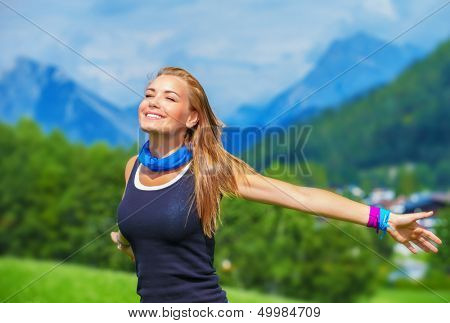 Portrait of happy traveler girl with raised up hands enjoying sunny day, mountains landscape, travel to Europe, happiness emotion, summer holiday concept