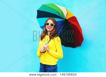 Happy Smiling Young Woman Holding Colorful Umbrella In Autumn Day Over Blue Background Wearing Yello